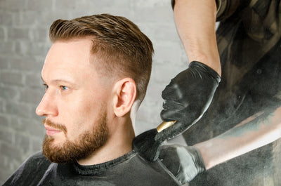 Man with thinning hair gets his hair cut as his barber brushes trimmed hairs from his neck